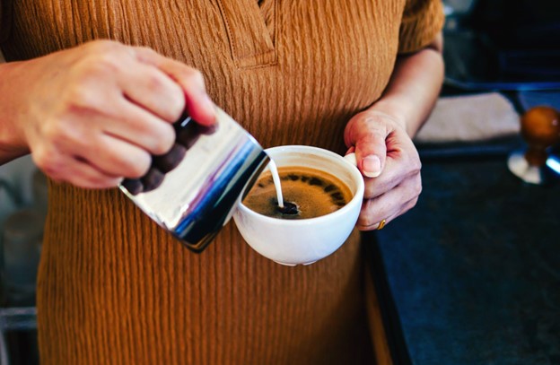 A person pouring milk into a cappuccino cup